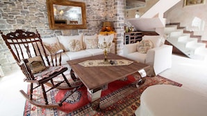 A living room with a stone wall, white sofas, a wooden rocking chair, and a staircase. - Villa Stella Adriatica (Tivat)