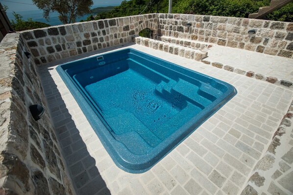 A rectangular hot tub with a stone wall surrounding it, set against a scenic backdrop.