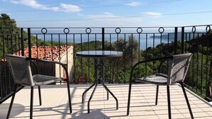 Un balcón con dos sillas de mimbre y una mesita redonda, con vistas a un paisaje marino y vegetación.