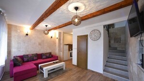 Una sala de estar moderna con techo de madera, un sofá rosa, una mesa de centro blanca y una escalera que sube a un nivel superior.
