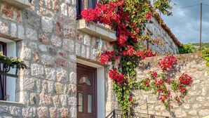 Un edificio de piedra con una puerta de madera, una escalera con barandilla negra y flores rojas trepando por la pared.