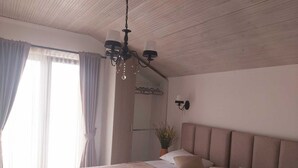 Een slaapkamer met een groot bed, een kroonluchter, een plant in pot en uitzicht op de omgeving.