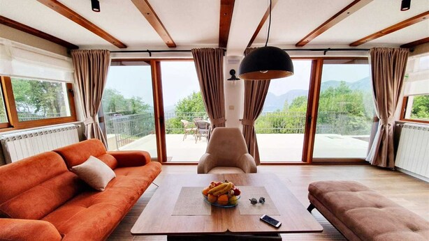 Een moderne woonkamer met een bank, een bijzettafeltje met fruit en uitzicht op het groen.