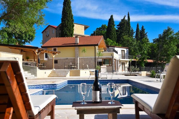 A poolside area with lounge chairs, a table with a bottle and glasses, and a view of a building with a red-tiled roof.