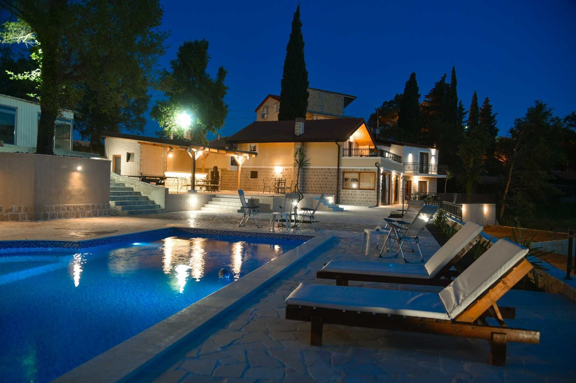 Ein zweistöckiges Haus mit Swimmingpool, Sitzgelegenheiten im Freien und einer gut beleuchteten Terrasse.