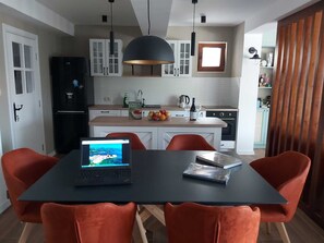 A modern kitchen with white cabinets, a black refrigerator, and a dining area with a laptop and a book on the table.