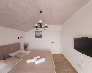 A bedroom with a bed, a chandelier, a painting, a television, and a door.