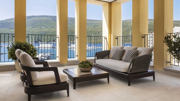 Un balcon aménagé avec un canapé, un fauteuil et une table basse, offrant une vue sur une étendue d’eau et la verdure.