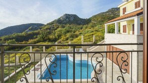 Una piscina con vistas a la montaña, un balcón con barandilla y un edificio con tejado de tejas.