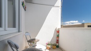 Een klein balkon met een witte stoel, een tafeltje en bloempotten.