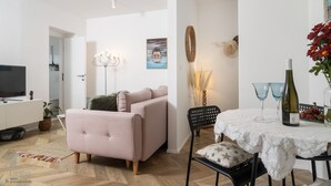 Een moderne woonkamer met een roze bank, een eettafel met een witte tafelkleed, en een televisie op een wit kastje.