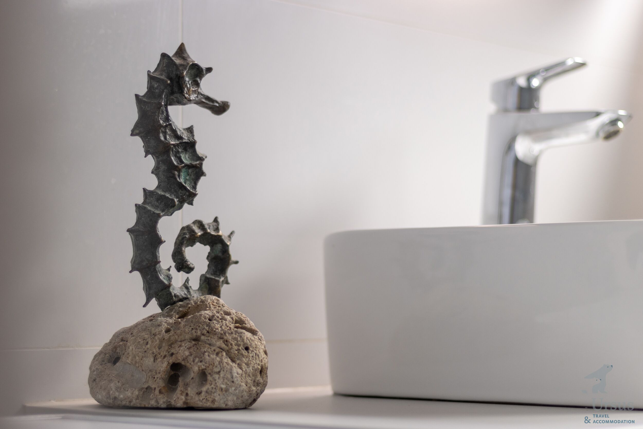 A bathroom with a white sink and a decorative seahorse sculpture on a rock.