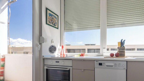 Een moderne keuken met een vaatwasser, oven en een raam met zonwering.