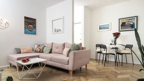 Een moderne woonkamer met een roze bank, een witte salontafel en een eethoek met een tafel en stoelen.