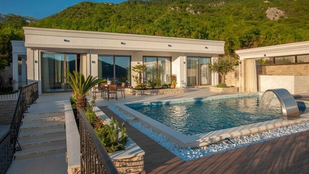 Eine moderne Villa mit Swimmingpool, Sitzgelegenheiten im Freien und Blick auf einen grünen Hügel.