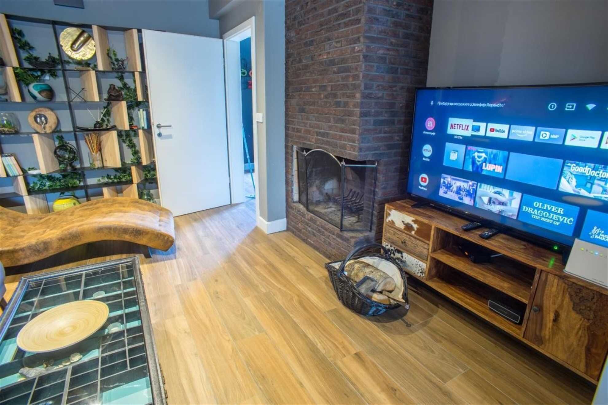 Uma sala de estar com lareira, uma TV de tela plana exibindo serviços de streaming e uma mesa de centro de madeira.
