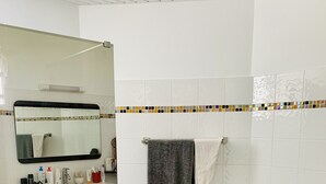 Een badkamer met een witte betegelde douche, een zwart wastafelmeubel met spiegel en een betegelde vloer.