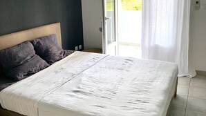 Een slaapkamer met een bed, een donkere muur, een raam met gordijnen en uitzicht op groen.