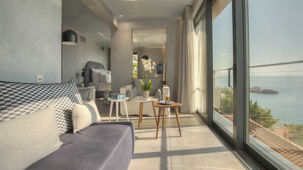 A balcony with a sofa, a small table, and a chair, overlooking a body of water and a bridge.