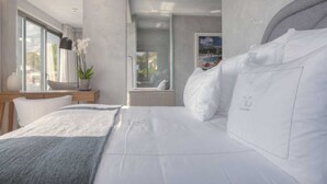 A modern hotel room with a large bed, a view of the pool, and a window with a plant on the nightstand.