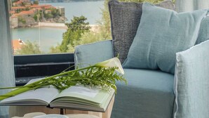A room with a view of a body of water, a blue sofa, an open book, and a bowl on a wooden table.