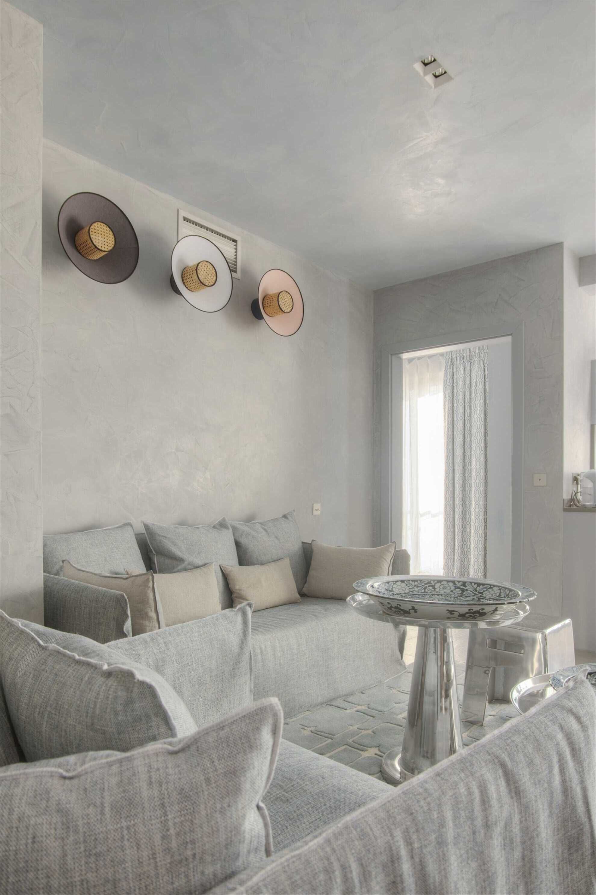 A modern living room with a grey sofa, a small round table, and wall-mounted light fixtures.