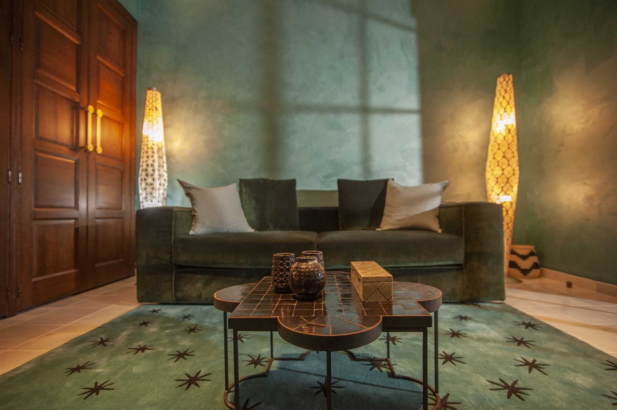Una habitación con un sofá verde oscuro, una alfombra estampada y una mesa de centro con adornos.