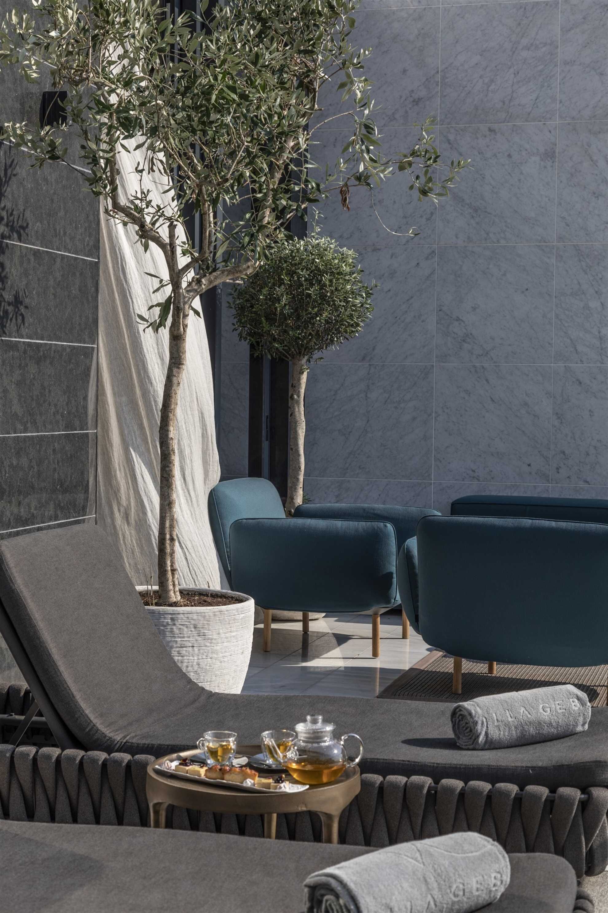 Un espace extérieur moderne aménagé avec une table préparée pour le thé, deux chaises et un arbre en pot.