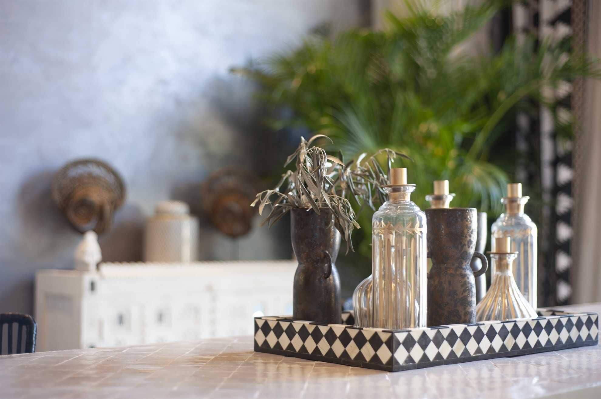 Une table sur laquelle se trouve un plateau noir et blanc orné de motifs, ainsi que plusieurs bouteilles en verre et un vase contenant des plantes séchées.