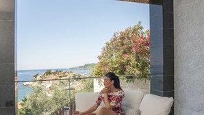 Una mujer sentada en un sofá redondo tejido para exteriores, con vista al mar y a un pueblo costero.
