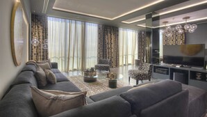 A modern living room with a sofa set, a glass coffee table, patterned curtains, and a television. - Villa Geba Suite Elena (Budva)