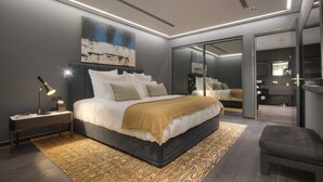 A modern bedroom with a large bed, bedside tables, a desk, and a mirror. - Villa Geba Suite Elena (Budva)