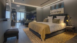 A modern bedroom with a large bed, bedside tables, a desk, and a view of the city. - Villa Geba Suite Elena (Budva)