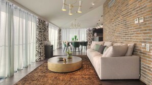 Un salon moderne avec un mur en briques, une table basse ronde, un canapé et, au fond, un coin repas.