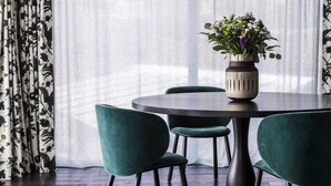 Un coin repas avec une table ronde, quatre chaises à l’assise rembourrée de couleur verte, un vase avec des fleurs et un lustre moderne.
