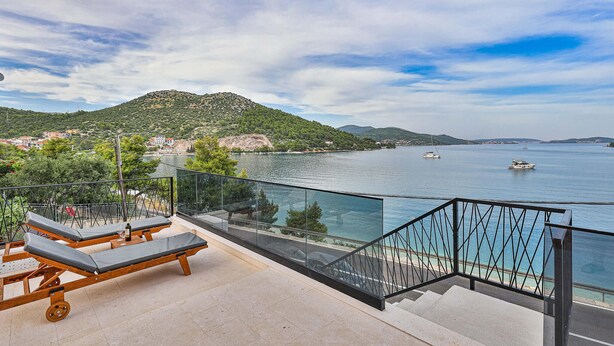 A balcony with sun loungers overlooking a body of water, a staircase, and a view of a hillside with buildings. - Beautiful apartment in Marina (Marina)