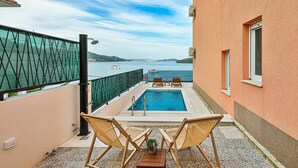A balcony with a pool, two wooden chairs, a small table, and a potted plant. - Beautiful apartment in Marina (Marina)