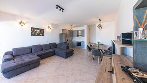 A modern living room with a sectional sofa, a dining area with a wooden table and chairs, and a kitchen in the background. - Beautiful apartment in Marina (Marina)