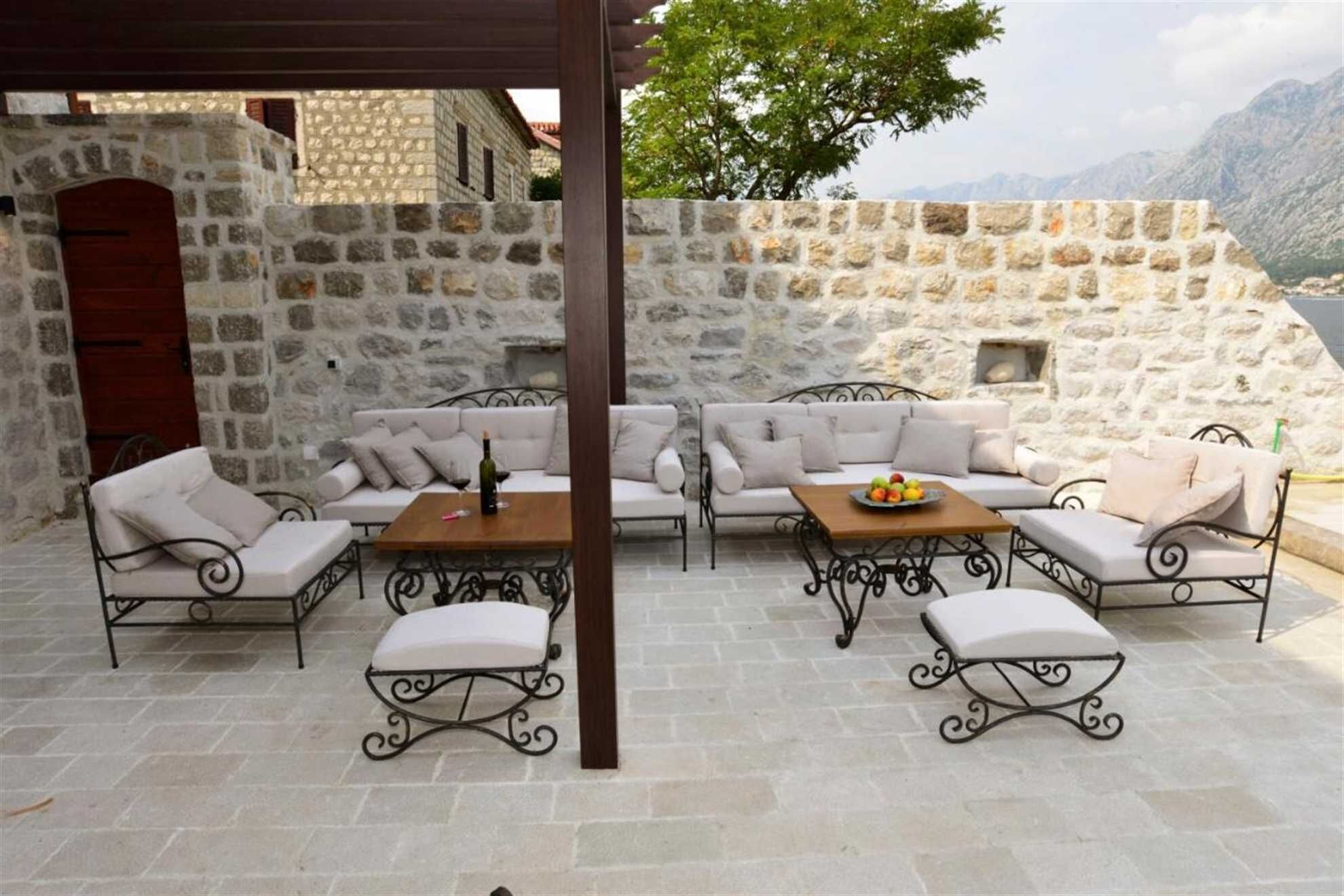 An outdoor seating area with stone walls, a wooden table, and cushioned chairs.