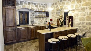 Cocina con armarios de madera, pared de piedra, barra con taburetes y encimera de piedra.