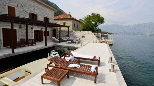Un hotel frente al agua con edificios de piedra, mesas al aire libre y un muelle.