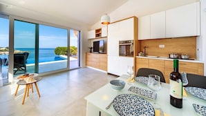 Een moderne keuken met uitzicht op zee, een eethoek met een gedekte tafel voor twee en een grote schuifpui die uitkomt op een buitenzitplaats.