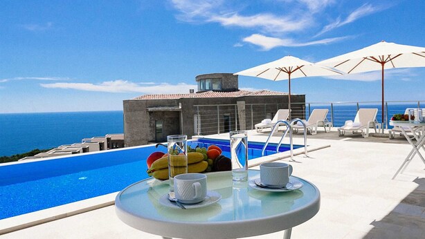 A poolside area with a clear view of the sea, a modern building, and lounge chairs. - Luxury Seaview Villa Krimovica 2 (Budva)
