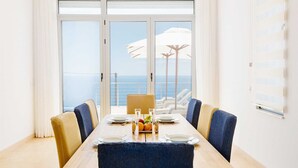A dining area with a view of the sea, a table set with plates and glasses, and a row of chairs. - Luxury Seaview Villa Krimovica 2 (Budva)