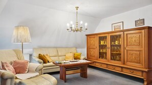 Una sala de estar con sofá, sillón, mesa de centro y aparador de madera con puertas de cristal.