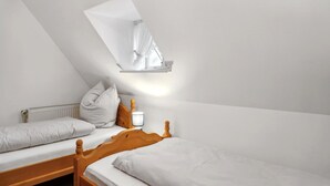Un dormitorio con dos camas, una ventana con cortina blanca y una mesita de noche con lámpara.