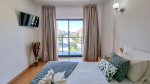A bedroom with a bed, a TV, a window with curtains, and a view of buildings outside.