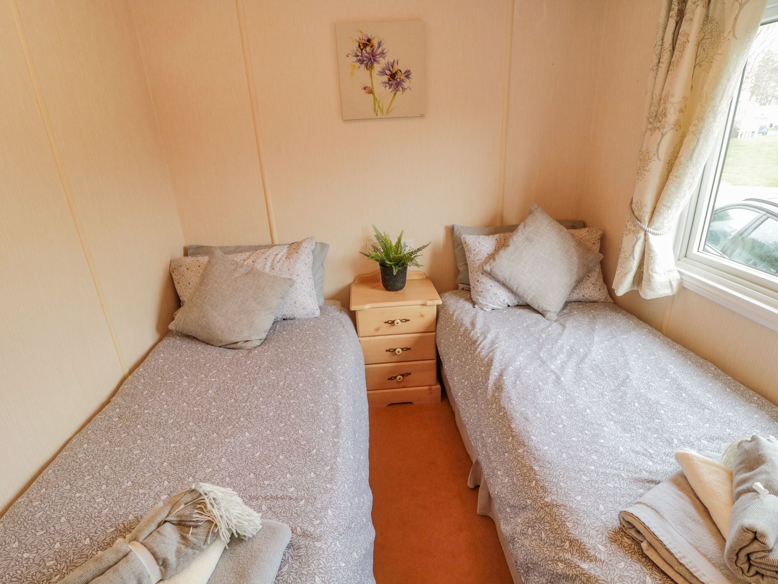 A twin room with two beds, a small bedside table with a plant, and a window with curtains.