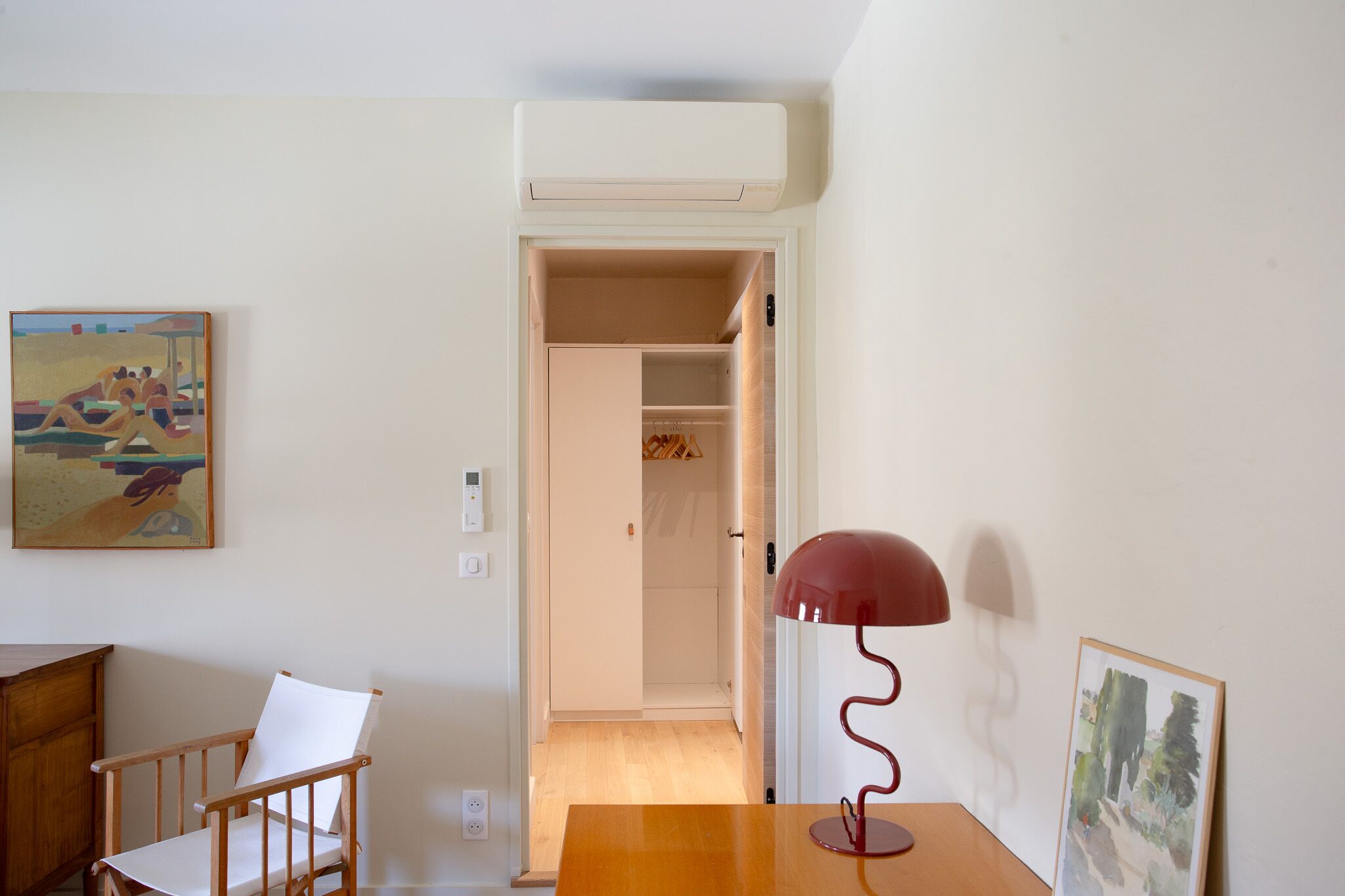 Una habitació amb una cadira de fusta, una taula, una làmpada vermella i un quadre a la paret.