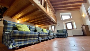 Un lungo divano blu a motivi tartan con cuscini verdi in una stanza con travi in legno e pavimento piastrellato.